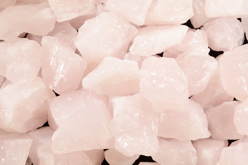 May include: A close-up of a pile of pink rose quartz crystals. The crystals are rough and have a natural, unpolished look.