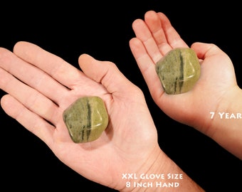 May include: Two hands holding a green and black striped stone. The stone is about the size of a golf ball. The hand on the left is an adult hand, and the hand on the right is a child's hand. The child's hand is labelled "7 year old". The adult hand is labelled "XXL Glove Size 8 inch Hand".