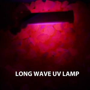 May include: A long wave UV lamp illuminating a pile of white rocks, causing them to glow a bright pink color. The text "LONG WAVE UV LAMP" is visible at the bottom of the image.