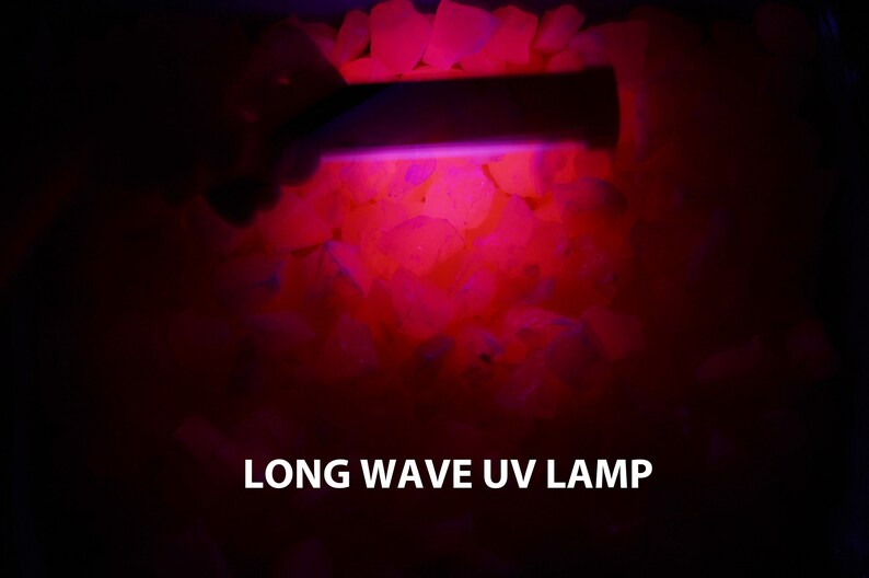 May include: A long wave UV lamp illuminating a pile of white rocks, causing them to glow a bright pink color. The text "LONG WAVE UV LAMP" is visible at the bottom of the image.