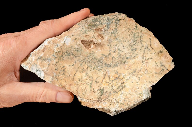 May include: A close-up of a light brown and green rock with a rough, uneven surface. The rock has a unique pattern of green veins running through it.