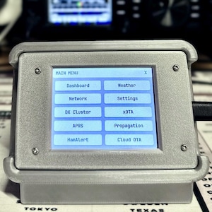 May include: A gray, 3D-printed electronic device with a rectangular touchscreen display showing a main menu with buttons labeled Dashboard, Weather, Network, Settings, DX Cluster, XOTA, APRS, Propagation, HamAlert, and Cloud OTA, with a black cable.