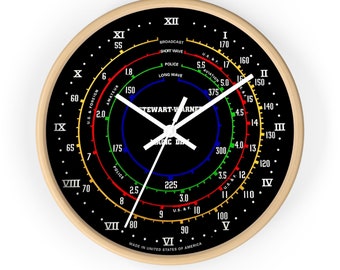 May include: A black and white clock face with a wooden frame. The clock face has multiple concentric circles with numbers and text, including "BROADCAST", "SHORT WAVE", "POLICE", "LONG WAVE", "AMATEUR", "U.S. & FOREIGN", "AVIATION", "U.S. & F.", "STEWART-WARNER", "MAGIC DIAL", and "MADE IN UNITED STATES OF AMERICA".