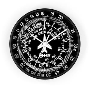 May include: Black and white aviation-themed wall clock. The clock face features a detailed design with markings for speed, distance, and time, including miles and kilometers. The clock hands point to the current time. The clock has a black frame.