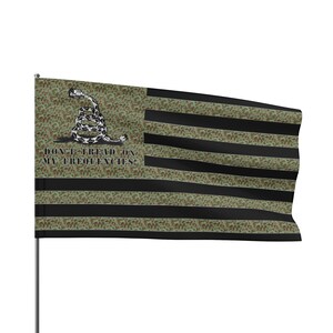May include: A green, black and white American flag with a snake and the text "Don't Tread On My Frequencies!" printed on it. The flag is made of a fabric material and is waving in the wind.