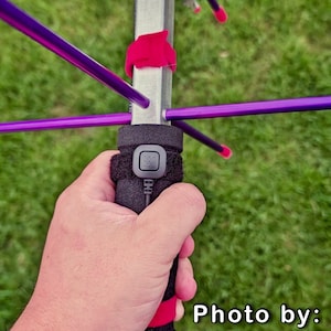 May include: A close-up of a silver antenna with purple rods and a black foam grip. The antenna has a red strap and a black button on the grip. Photo by: KH6WI