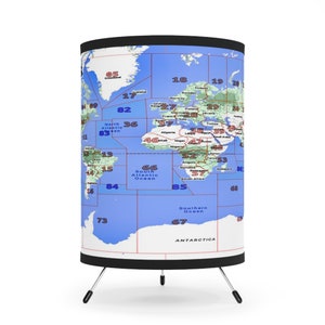 May include: A world map printed on a cylindrical lampshade with red and blue lines dividing the map into numbered sections. The lampshade is mounted on a black tripod stand.