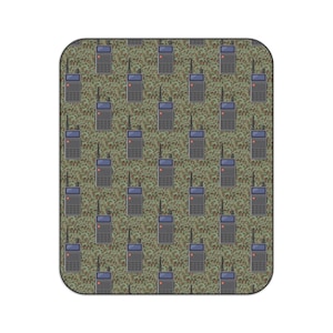 Puede incluir: Una alfombra rectangular con un patrón repetido de walkie-talkies grises con antenas negras y luces rojas. El fondo es un diseño de camuflaje en tonos verdes, marrones y beige. La alfombra tiene esquinas redondeadas.
