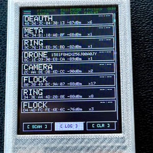 May include: A handheld electronic device with a white 3D-printed case and a black screen displaying a list of network signals including DEAUTH, META, RING, DRONE, CAMERA, and FLOCK, with buttons labeled SCAN, LOG, and CLR at the bottom.