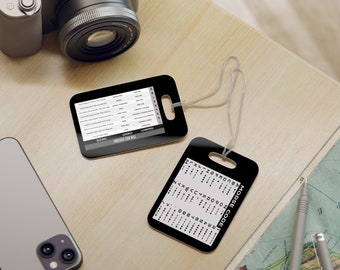 May include: Two black plastic luggage tags with white text. One tag has the Morse code alphabet and the other tag has the text "The Dot System" and a table of dots and dashes.