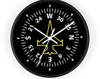 May include: Black clock face with white markings and a yellow airplane silhouette in the center. The clock face has numbers from 1 to 30 and the letters N, S, E, and W.