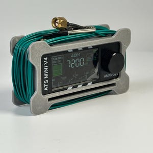 Puede incluir: Una radio ATS MINI V4 plateada y negra con una pantalla digital que muestra la frecuencia 7200. La radio tiene una perilla negra y está envuelta con cable verde. Una antena está unida en la parte superior.