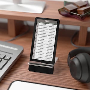 Könnte beinhalten: Ein schwarzer Smartphone-Ständer mit einem weißen Bildschirm, auf dem eine Tabelle mit Q-Codes angezeigt wird. Die Tabelle listet den Code, den Code, der als Frage verwendet wird, und den Code, der als Aussage verwendet wird. Der Ständer steht auf einer Holzoberfläche mit einer Tastatur und Kopfhörern.