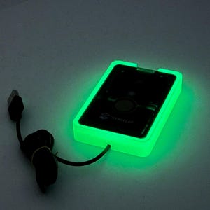May include: A glowing green rectangular device with a black screen and a black cord with a USB connector. The device has a bright green border and the text "SENSECAP" is visible on the screen.
