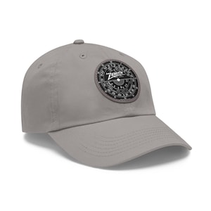 Puede incluir: Una gorra de béisbol gris con un parche negro y blanco de dial de radio Zenith en la parte delantera.