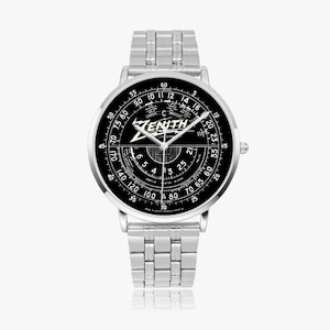 May include: A silver-toned Zenith wristwatch with a black face featuring white numerals and markings. The watch has a stainless steel band and a round watch face with the Zenith logo and text. The watch face displays various scales and measurements.