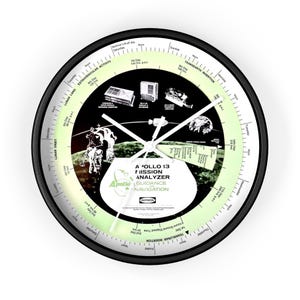 May include: A black and white clock with a green background. The clock face features a graphic of the Apollo 13 mission, including the text "Apollo 13 Mission Analyzer Guidance Navigation". The clock hands are white.