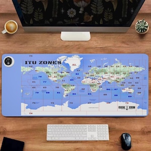May include: A blue rectangular desk mat featuring a world map with ITU zones labeled. The mat has a light blue border and includes a white keyboard, a black mouse, and a small control panel on the left side. The text "ITU ZONES" is visible.