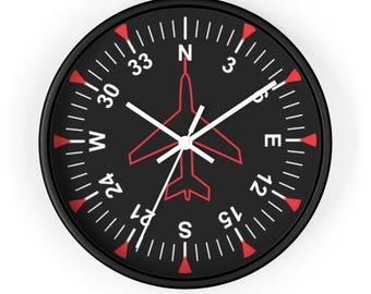 May include: Black clock face with red markings and white numbers. The clock face has a compass design with a red airplane in the center. The clock hands are white.