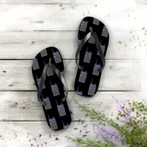 Puede incluir: Un par de chanclas negras con un patrón de walkie talkies. Las chanclas están sobre una superficie de madera.