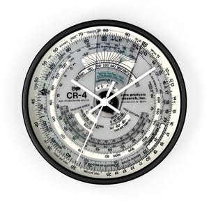 May include: A black and white circular clock with a silver face and black hands. The clock face has various aviation-related scales and markings, including true air speed, true altitude, and temperature. The clock face also includes the text "aero products research, inc. Los Angeles, CA 1974" and "CR-4".