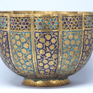 Peut inclure: Un bol en métal doré avec un bord festonné et des motifs floraux ajourés sur le dessus. L'extérieur est orné de panneaux alternés de motifs floraux bleus et dorés, mettant en valeur des gravures détaillées et des accents de type émail.