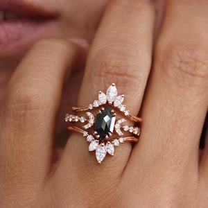 May include: A three-piece rose gold engagement ring set with a black diamond centre stone and a delicate floral design.