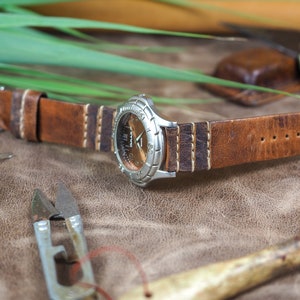 May include: A brown leather watch strap with white stitching. The strap is attached to a silver watch with a round face.