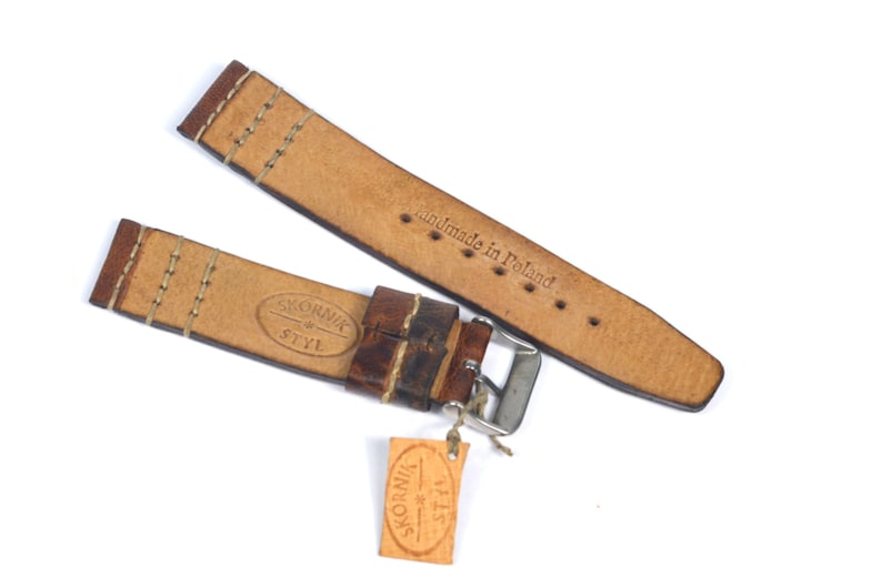May include: Brown leather watch strap with white stitching and a silver buckle. The strap is labeled "Sk&oacute;rnik Styl" and "handmade in Poland".