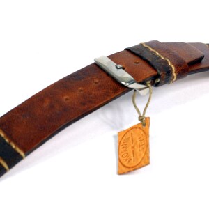 May include: Brown leather watch strap with white stitching and a silver buckle. The strap has a small leather tag attached with the text "THIS IS VINNAGE".