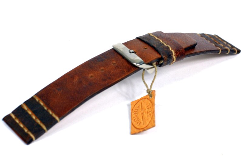May include: Brown leather watch strap with white stitching and a silver buckle. The strap has a small leather tag attached with the text "THIS IS VINNAGE".