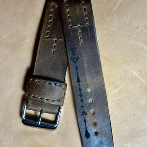 May include: Two brown leather watch straps with white stitching and a silver buckle. One strap features a series of black symbols and arrows. The leather has a distressed appearance.