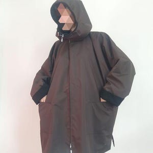 May include: A brown hooded jacket with a zipper closure and two pockets. The jacket has a black lining around the hood and the cuffs.