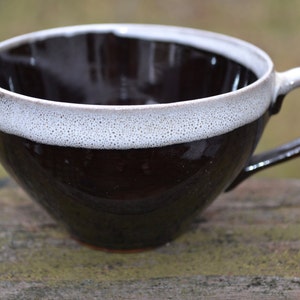 Może przedstawiać: Ręcznie wykonany ceramiczny kubek do kawy z ciemnobrązowym zewnętrzem i białym, nakrapianym brzegiem. Kubek ma duży uchwyt i szeroki otwór. Odpowiedni do gorących lub zimnych napojów. Wymiary w centymetrach.