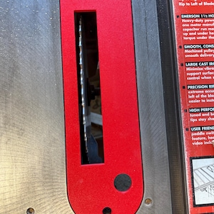 May include: Close-up of a red and silver table saw with a blade exposed. The saw has a large cast iron base and a precision rip fence. The text on the saw reads "EMERSON 1 1/2 HP Heavy-duty power with one motor manufactured with a capacitor run motor. Smooth, consistent torque under the heavy load."