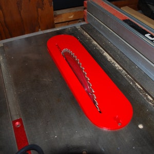 May include: A red table saw blade guard with a silver blade inside. The guard is mounted on a black table saw.