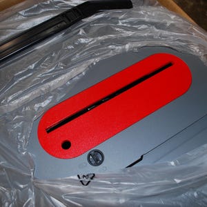 May include: A gray and red circular saw blade with a black plastic handle. The blade is covered in a clear plastic bag.