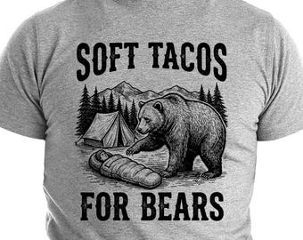Puede incluir: Camiseta gris con un diseño negro que muestra un oso, una tienda de campaña y el texto "SOFT TACOS FOR BEARS". El oso se acerca a un saco de dormir. El diseño está ambientado en un fondo de árboles y montañas.