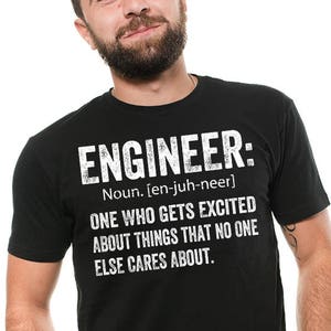 May include: A black t-shirt with white text that reads "ENGINEER: Noun. [en-juh-neer] ONE WHO GETS EXCITED ABOUT THINGS THAT NO ONE ELSE CARES ABOUT."
