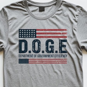 May include: A gray t-shirt with a distressed American flag design and the text "D.O.G.E. DEPARTMENT OF GOVERNMENT EFFICIENCY".
