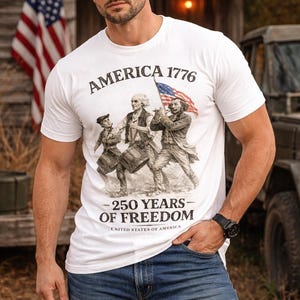 May include: White t-shirt with the text "AMERICA 1776 - 250 YEARS OF FREEDOM" and a graphic of historical figures carrying a flag. The person is wearing a brown cap and blue jeans. An American flag is in the background.