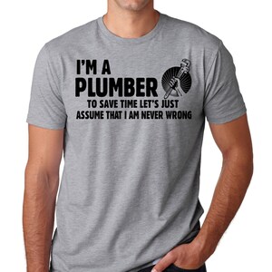 May include: A gray t-shirt with the text "I'M A PLUMBER TO SAVE TIME LET'S JUST ASSUME THAT I AM NEVER WRONG" in black. The shirt also features a graphic of a hand holding a wrench.
