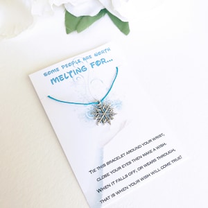 May include: A silver snowflake charm bracelet on a white card with the text "SOME PEOPLE ARE WORTH MELTING FOR...". The card also includes instructions on how to make a wish. The bracelet is tied with a turquoise string.