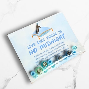 May include: A card with the text "LIVE LIKE THERE IS NO MIDNIGHT" and a blue pillow illustration. The card is packaged with a variety of blue and clear beads. The beads are in various shapes and sizes.