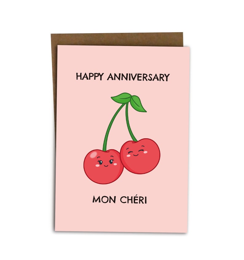 Puede incluir: Una tarjeta rosa con el texto "Happy Anniversary" y "Mon Ch&eacute;ri" con una imagen de dibujos animados de dos cerezas rojas con caras sonrientes.