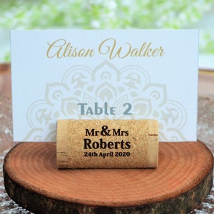 Personalized engraved horizontal wine cork, number 19 design, used for rustic wedding place cards, wedding place holder, parties and table decoration. on a wooden base with decorative flowers. Gift for guests, beautiful decoration for weddings.