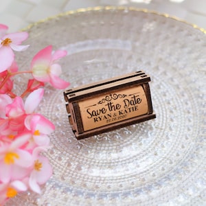 Personalized Save the Date corks for wine with wooden box and with or without magnets, used in wine themed weddings, and rustic weddings. It is made of 100% Natural High Quality Cork. On a glass plate with decorative flowers.