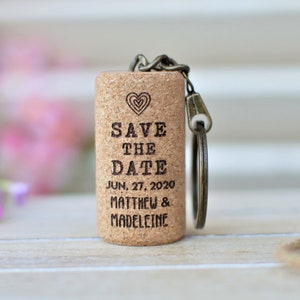 May include: A cork keychain with a heart and the text "Save the Date" engraved on it. The date "Jun. 27, 2020" and the names "Matthew & Madeleine" are also engraved on the cork.
