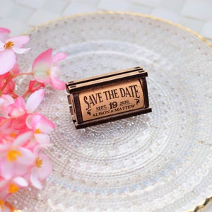 Personalized Save the Date corks for wine with wooden box and with or without magnets, used in wine themed weddings, and rustic weddings. It is made of 100% Natural High Quality Cork. On a glass plate with decorative flowers.