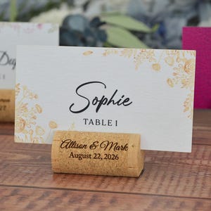 Personalized cork card holder, used for place cards for rustic style weddings, wedding favors, anniversaries, parties and birthdays. On a wooden base with decorative flowers. A beautiful decoration for weddings.